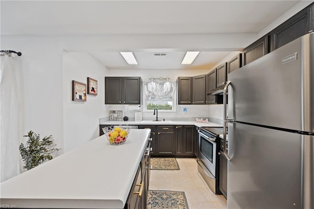 kitchen with under cabinet range hood, stainless steel appliances, a sink, light countertops, and a center island