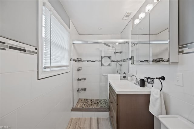 bathroom featuring toilet, visible vents, vanity, tile walls, and a shower stall