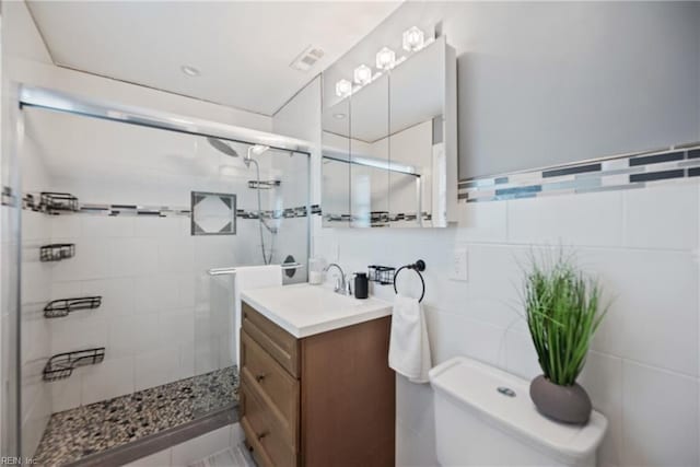 full bathroom featuring toilet, vanity, visible vents, tile walls, and a stall shower