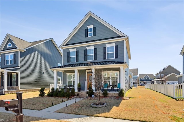 view of front facade with covered porch, a standing seam roof, fence, metal roof, and a front lawn