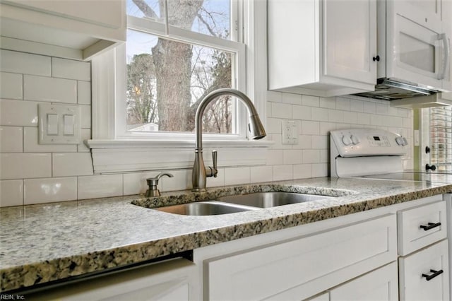 kitchen with white appliances, light stone counters, white cabinets, and a sink