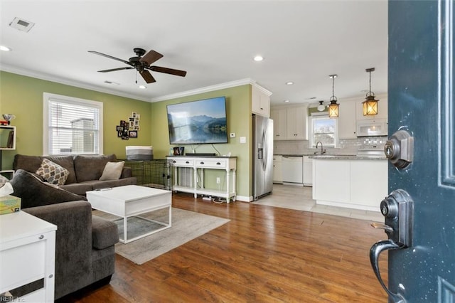 living room with visible vents, a ceiling fan, ornamental molding, light wood-type flooring, and recessed lighting