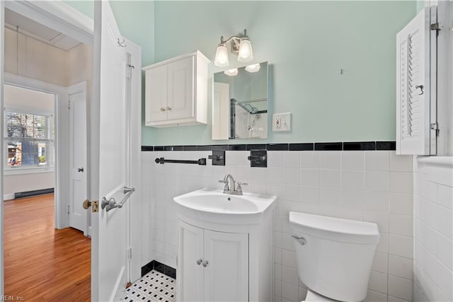 bathroom featuring toilet, wood finished floors, vanity, tile walls, and wainscoting