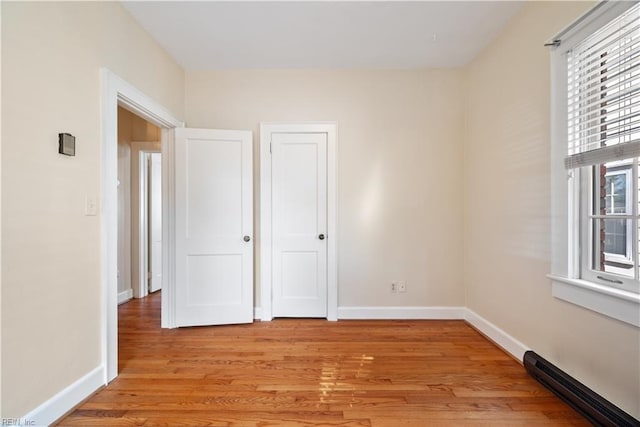 unfurnished bedroom featuring a baseboard heating unit, light wood-style flooring, and baseboards