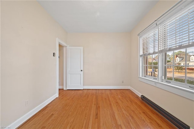 spare room with a baseboard heating unit, light wood-style floors, and baseboards