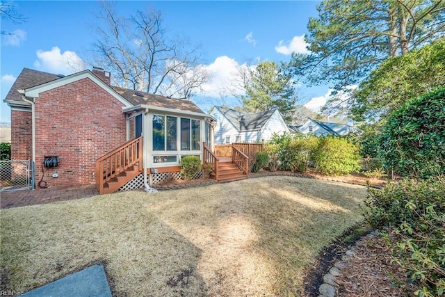 rear view of property with brick siding, a chimney, a lawn, a sunroom, and fence