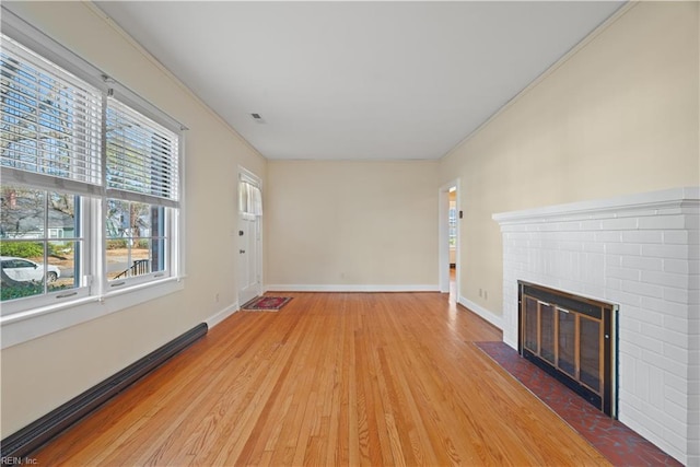 unfurnished living room featuring light wood finished floors, baseboard heating, a fireplace, and baseboards