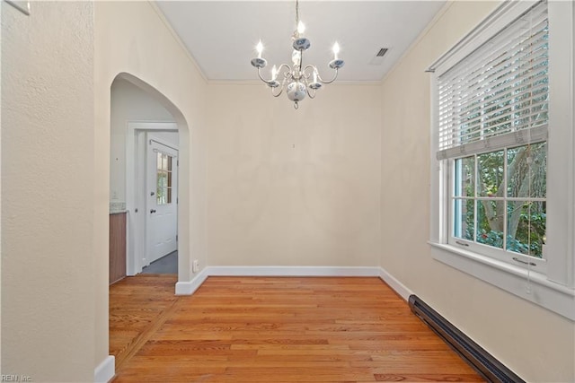 unfurnished dining area featuring arched walkways, light wood finished floors, baseboard heating, and crown molding