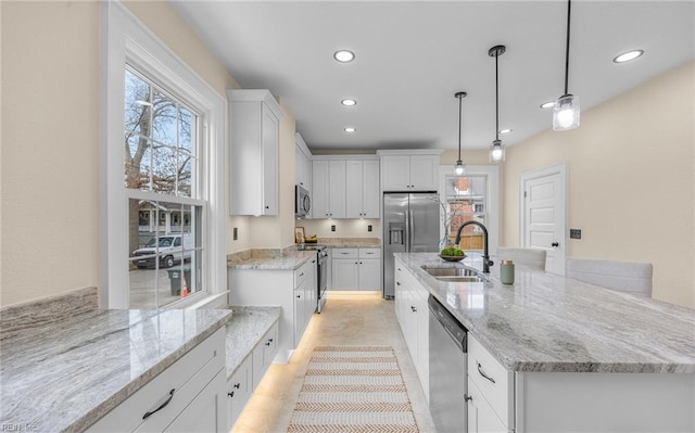 kitchen featuring stainless steel appliances, a sink, white cabinets, light stone countertops, and a center island with sink