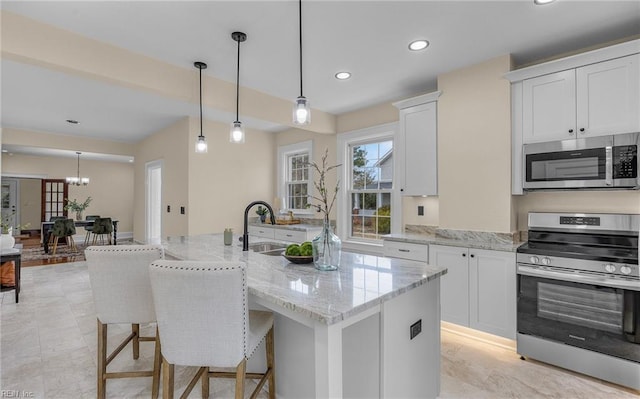 kitchen featuring white cabinets, light stone counters, appliances with stainless steel finishes, hanging light fixtures, and a sink