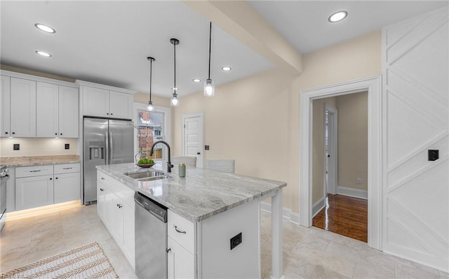 kitchen featuring a sink, white cabinetry, hanging light fixtures, appliances with stainless steel finishes, and light stone countertops