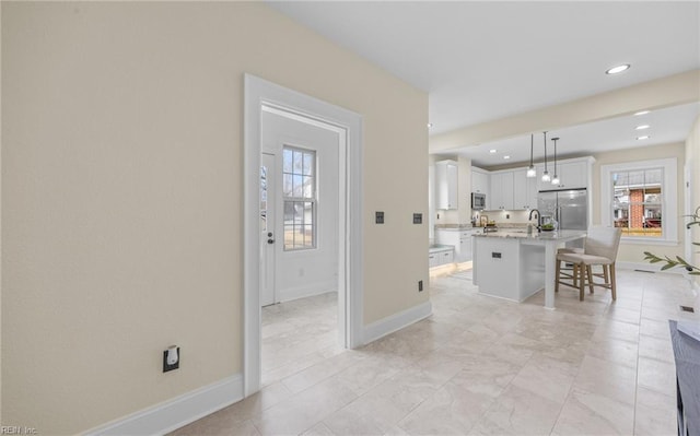 kitchen featuring an island with sink, appliances with stainless steel finishes, a breakfast bar, hanging light fixtures, and white cabinetry