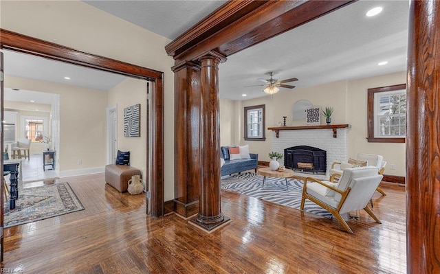 living area with a fireplace, baseboards, decorative columns, and hardwood / wood-style floors