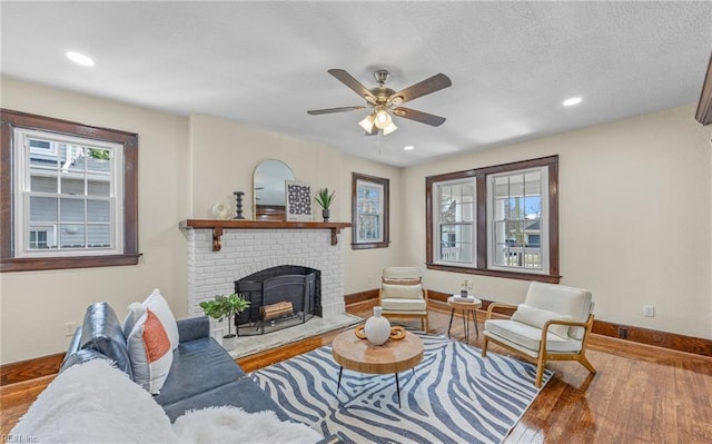 living area featuring a textured ceiling, hardwood / wood-style flooring, recessed lighting, baseboards, and a brick fireplace