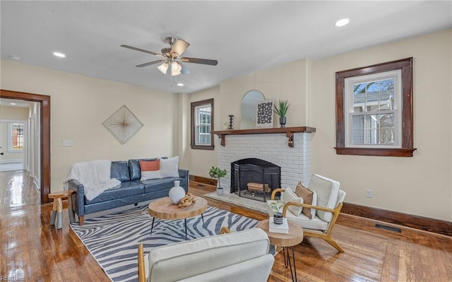 living area with visible vents, baseboards, ceiling fan, wood finished floors, and a brick fireplace