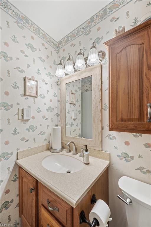 bathroom featuring toilet, wallpapered walls, and vanity