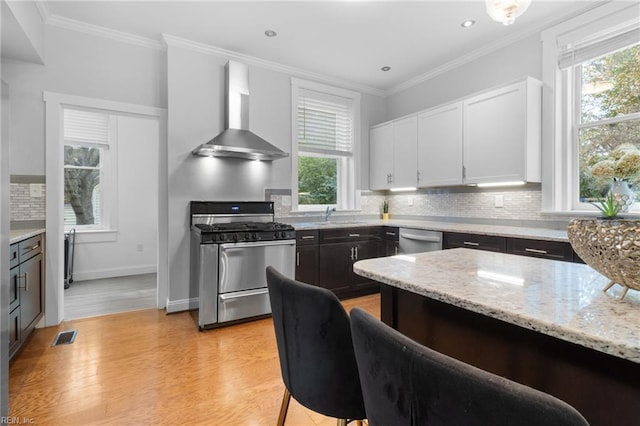 kitchen with wall chimney range hood, appliances with stainless steel finishes, decorative backsplash, and crown molding