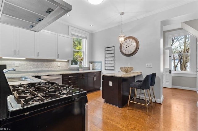 kitchen featuring light stone counters, ornamental molding, a sink, dishwasher, and wall chimney exhaust hood