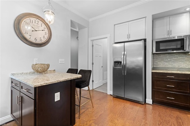 kitchen featuring crown molding, tasteful backsplash, appliances with stainless steel finishes, wood finished floors, and a kitchen bar