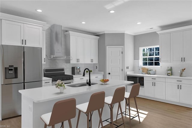 kitchen featuring a sink, range with gas stovetop, wall chimney range hood, stainless steel fridge with ice dispenser, and a kitchen bar