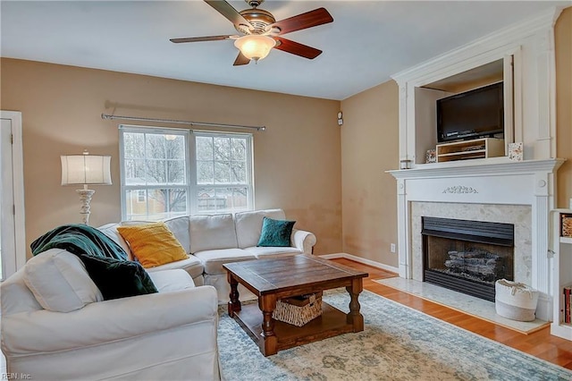 living area featuring ceiling fan, a fireplace, baseboards, and wood finished floors