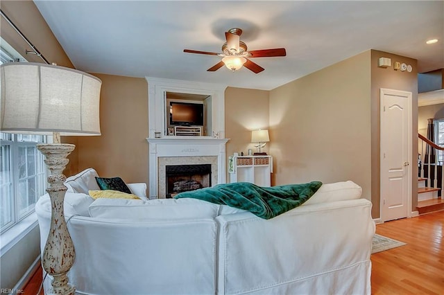 living room with stairs, ceiling fan, light wood finished floors, and a fireplace