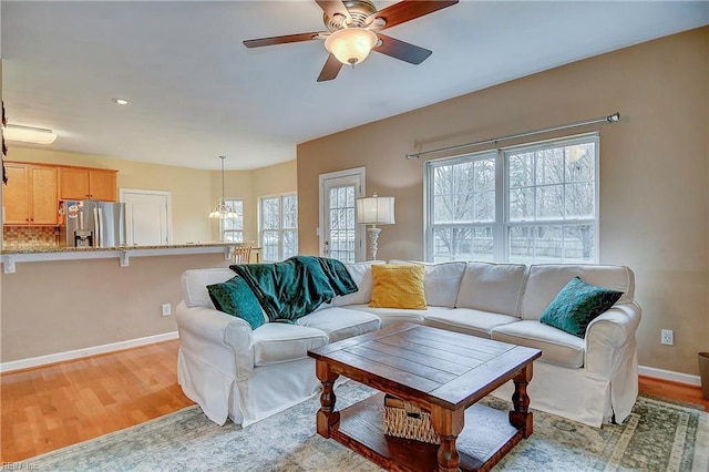 living area with light wood-style floors, ceiling fan, and baseboards