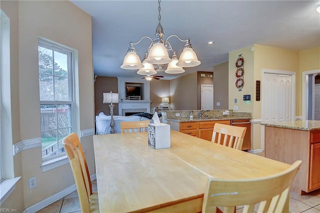 dining space featuring light tile patterned floors, a fireplace, baseboards, and ceiling fan with notable chandelier