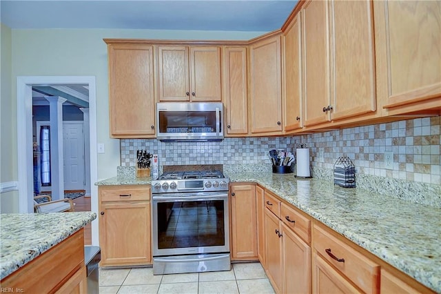 kitchen with light tile patterned floors, light stone counters, appliances with stainless steel finishes, tasteful backsplash, and decorative columns