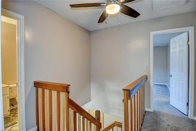 hallway with visible vents, a textured ceiling, carpet, and an upstairs landing