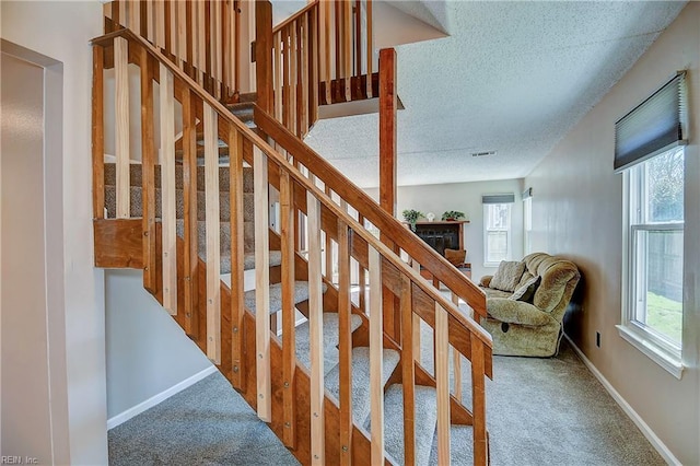 stairway featuring plenty of natural light, a textured ceiling, and carpet flooring