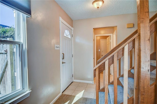 entryway featuring a textured ceiling, stairs, light tile patterned floors, and a wealth of natural light