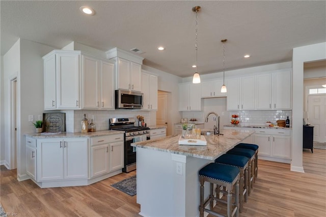 kitchen featuring appliances with stainless steel finishes, light wood-type flooring, white cabinetry, and light stone countertops