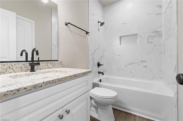 bathroom featuring toilet, a textured wall, shower / bath combination, and vanity