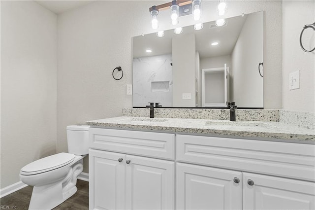 full bathroom with toilet, double vanity, baseboards, and a sink