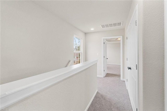 corridor with visible vents, baseboards, a textured wall, carpet, and an upstairs landing