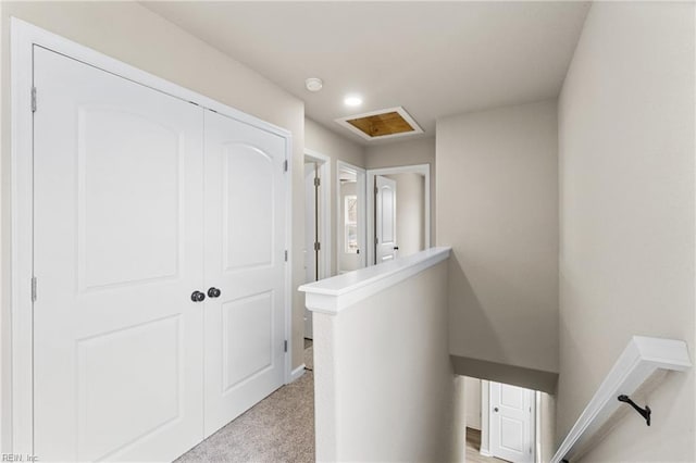 hallway with light carpet, attic access, and an upstairs landing