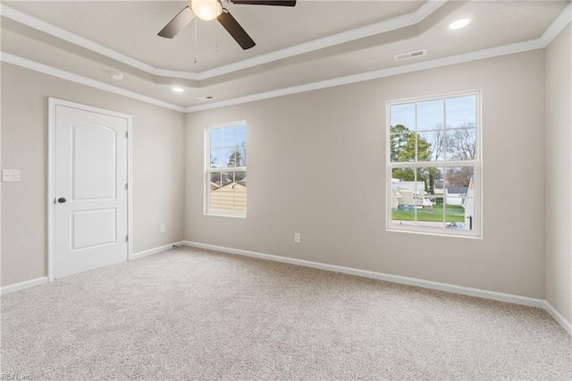 carpeted spare room featuring baseboards, visible vents, a tray ceiling, and crown molding