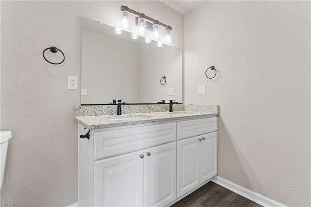 bathroom featuring double vanity, wood finished floors, a sink, and baseboards