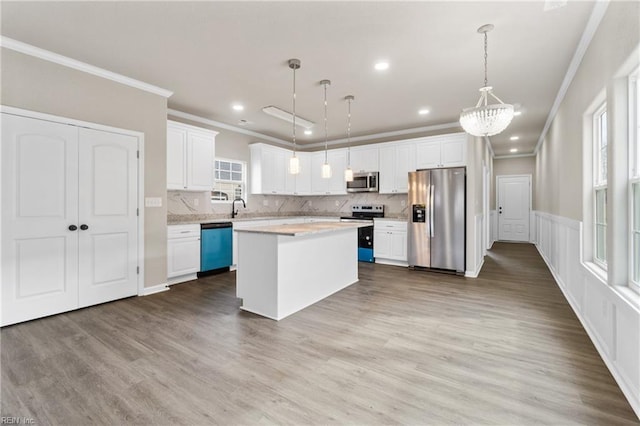 kitchen with a kitchen island, wood finished floors, stainless steel appliances, light countertops, and white cabinetry