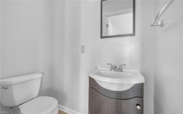 half bathroom featuring toilet, vanity, and baseboards