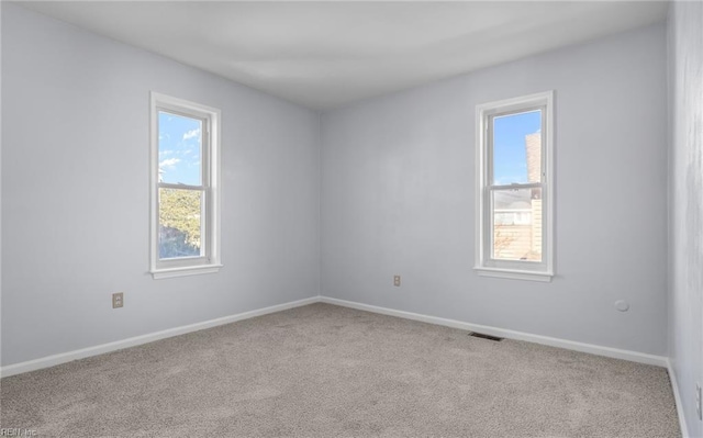 empty room with carpet, visible vents, and baseboards