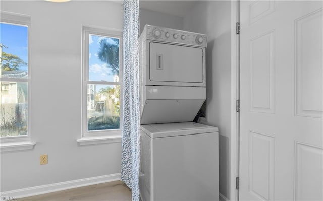 laundry room with laundry area, wood finished floors, stacked washer and clothes dryer, and baseboards