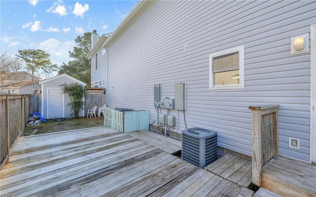 wooden deck with central air condition unit, fence, a storage unit, and an outbuilding