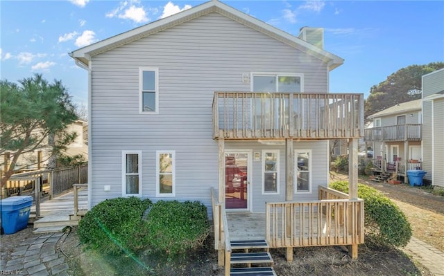 rear view of house featuring a balcony, a chimney, and a wooden deck