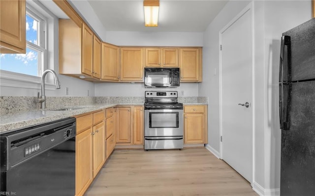 kitchen with light stone counters, light wood finished floors, light brown cabinets, a sink, and black appliances