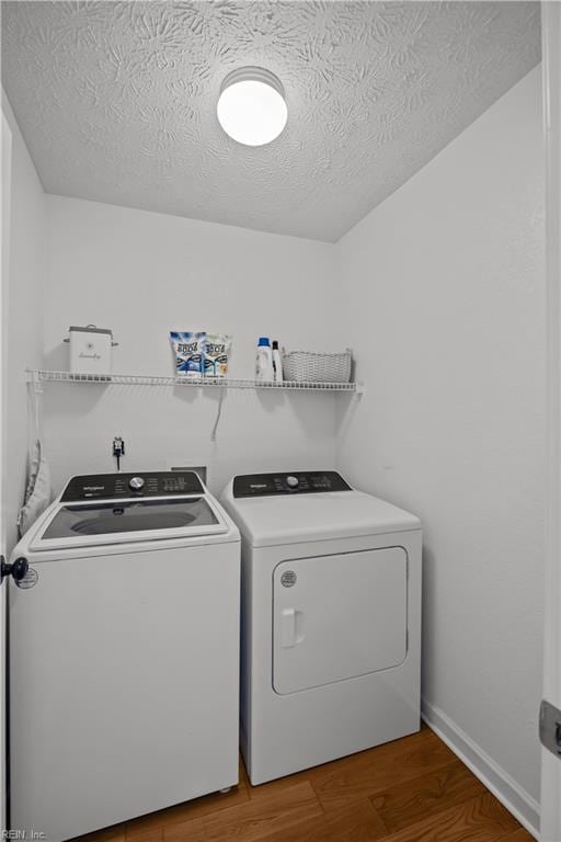 clothes washing area with a textured ceiling, laundry area, independent washer and dryer, and wood finished floors