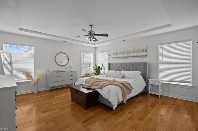 bedroom with light wood-style floors, baseboards, a tray ceiling, and a ceiling fan