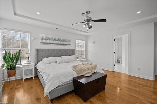 bedroom featuring light wood-style flooring, a tray ceiling, and baseboards