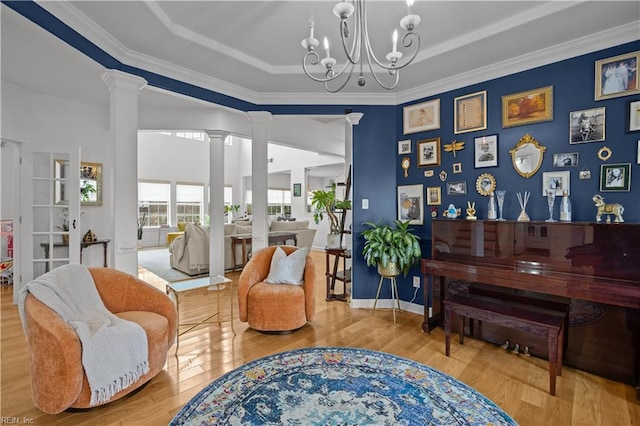 living area featuring a chandelier, wood finished floors, baseboards, a tray ceiling, and decorative columns